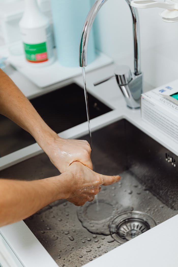 Hands being washed under running water in a modern stainless steel sink, promoting hygiene.