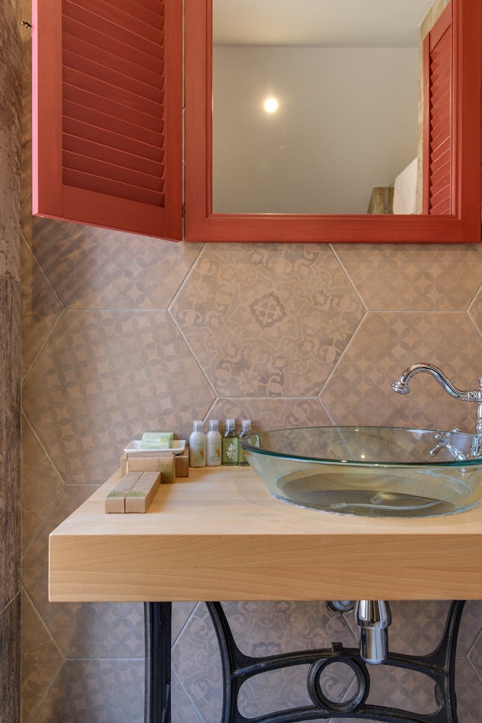 Elegant bathroom vanity featuring a glass basin and red shutter-style mirror.